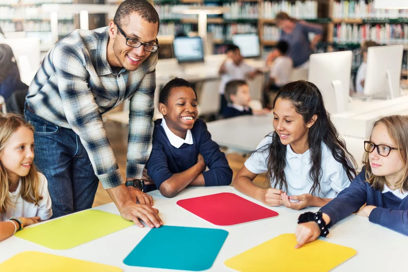 Man with glasses helping group of diverse students sitting at a table