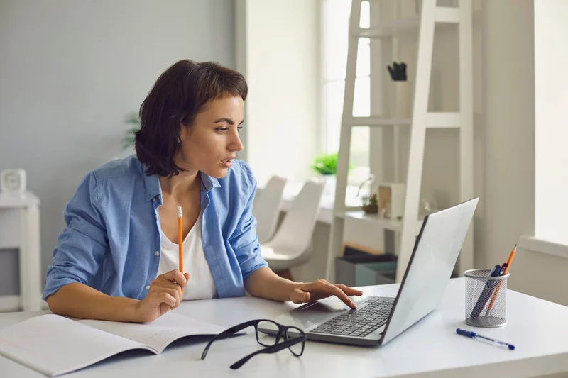 woman sitting at desk working at a laptop with a pencil and notebook